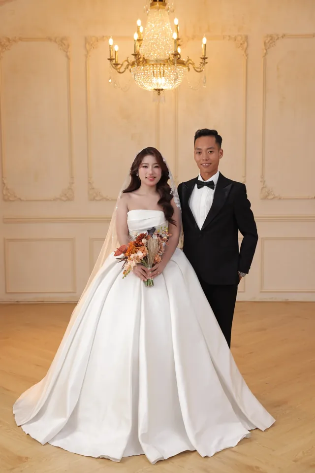 Khoa và Phương đứng giữa sảnh tiệc màu vàng ấm