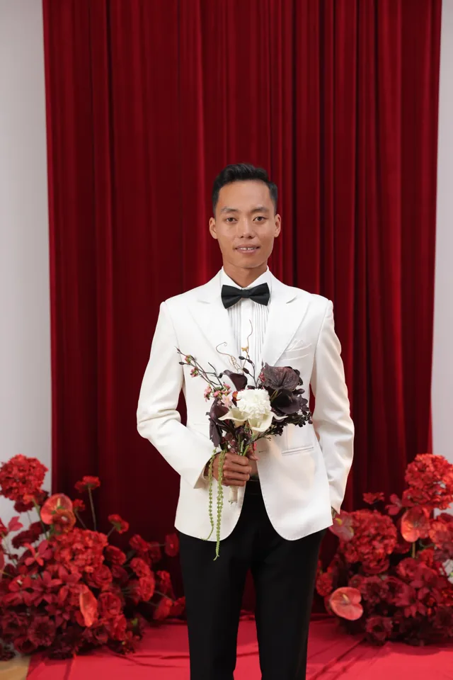 Lê Khoa mặc vest trắng trước phông hoa đỏ