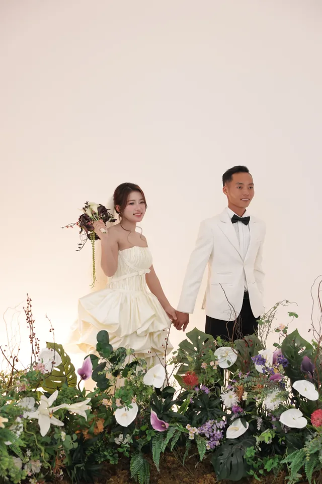 Khoa và Phương nắm tay giữa hoa trắng và lá xanh